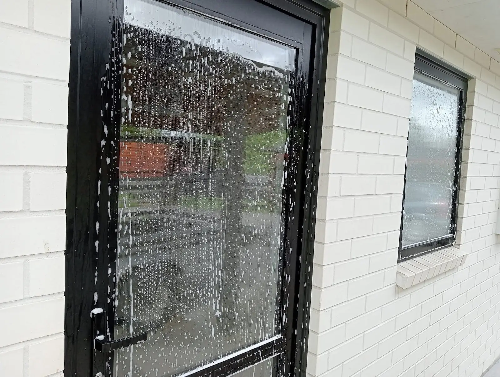A black framed glass door covered in soapy water, part way through a clean